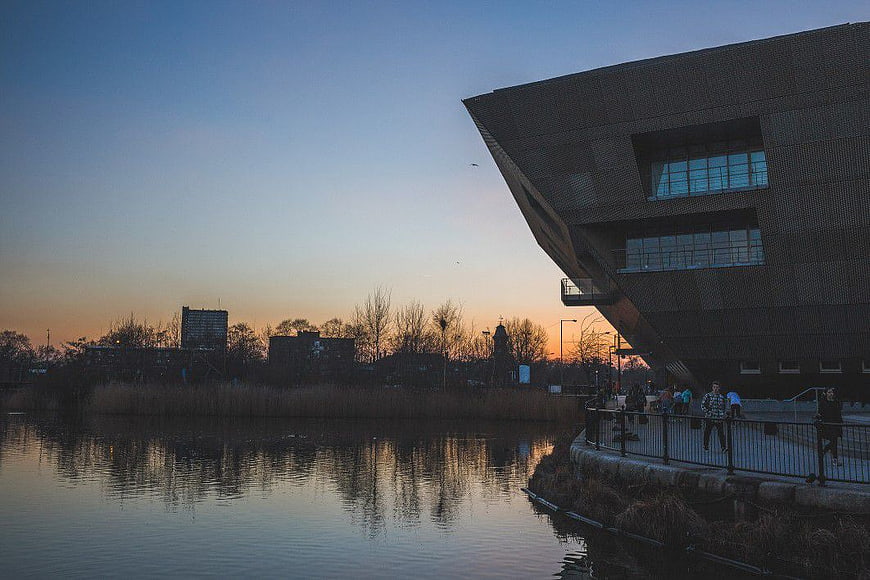 Modern angular building by river at sunset