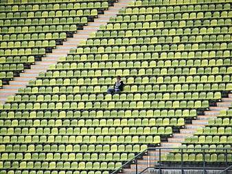 Lone person sitting in empty green stadium seats