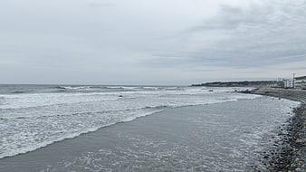 Overcast Rocky Beach with Ocean Waves and Coastal Buildings