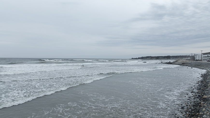Overcast Rocky Beach with Ocean Waves and Coastal Buildings
