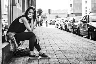 Black and white portrait of a young woman sitting on a city sidewalk
