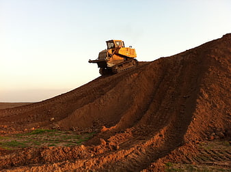 Yellow Bulldozer Grading Earth Mound at Sunset