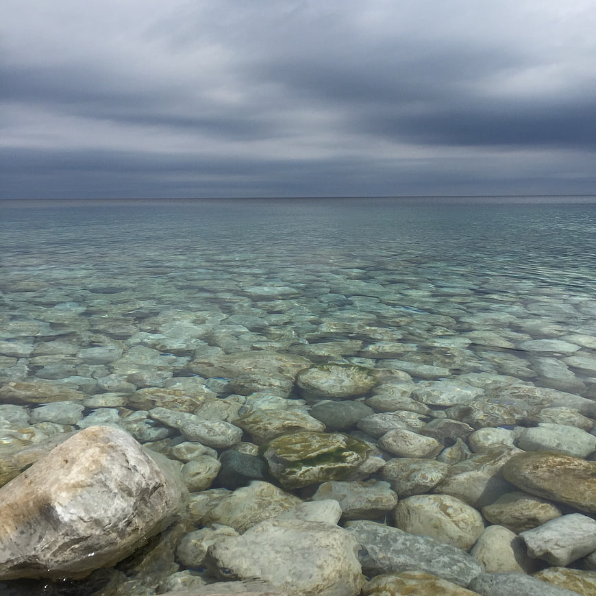 Clear shallow water over smooth stones under cloudy sky