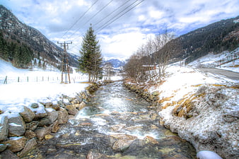 Winter mountain stream flowing through snowy valley with power lines