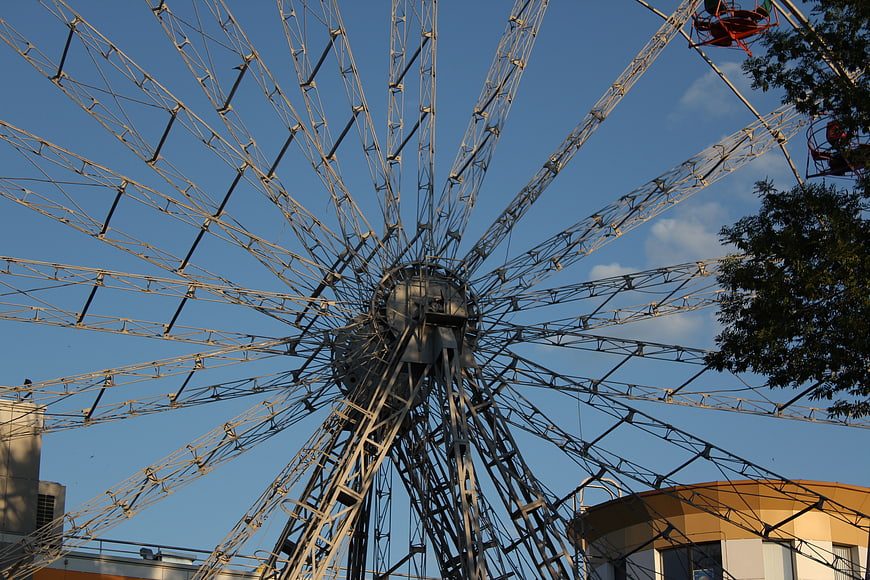 Low angle view of large steel ferris wheel against blue sky