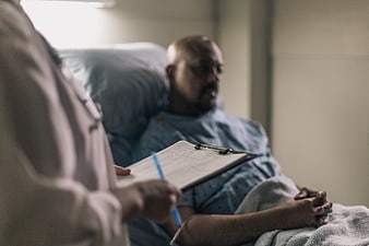 Doctor Taking Notes While Patient Rests in Hospital Bed
