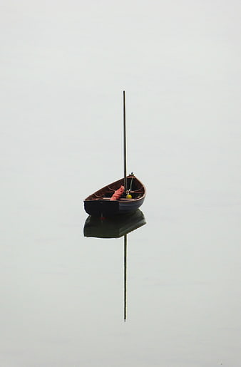 Solitary wooden boat with mast floating on calm misty water