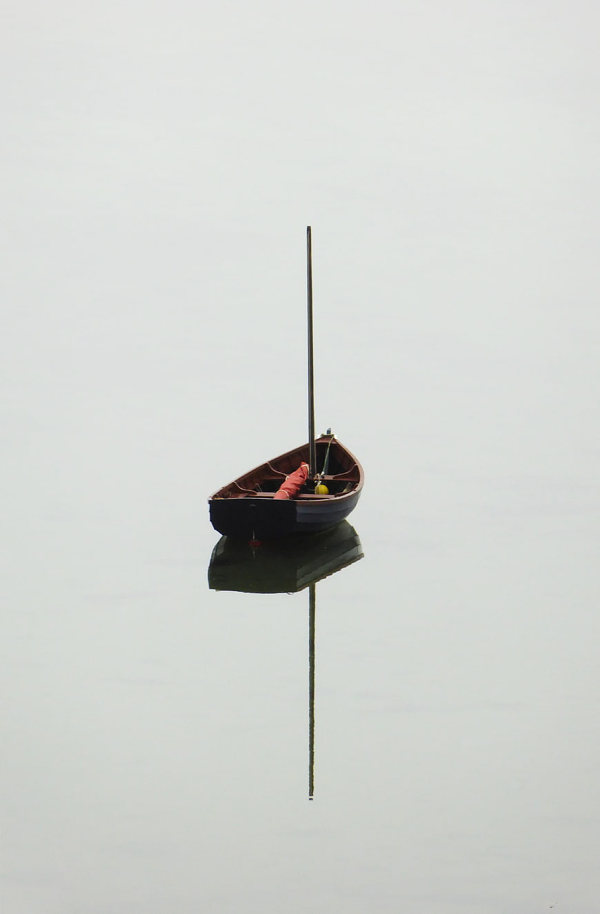 Solitary wooden boat with mast floating on calm misty water