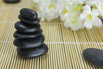 Stacked black zen stones on bamboo mat with white flowers