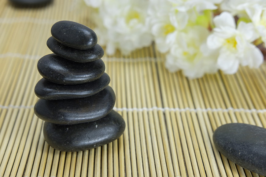 Stacked black zen stones on bamboo mat with white flowers