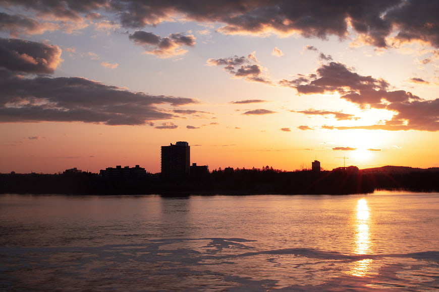 Silhouetted city skyline at sunset over icy river