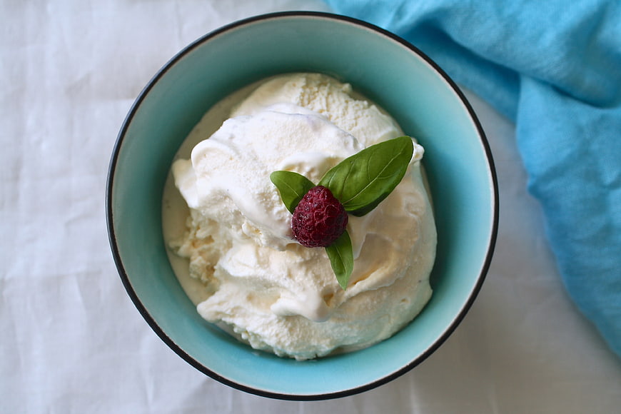 Overhead view of vanilla ice cream in a blue bowl with raspberry