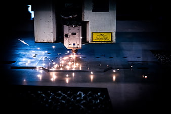 Industrial laser cutting machine creating bright sparks on metal sheet