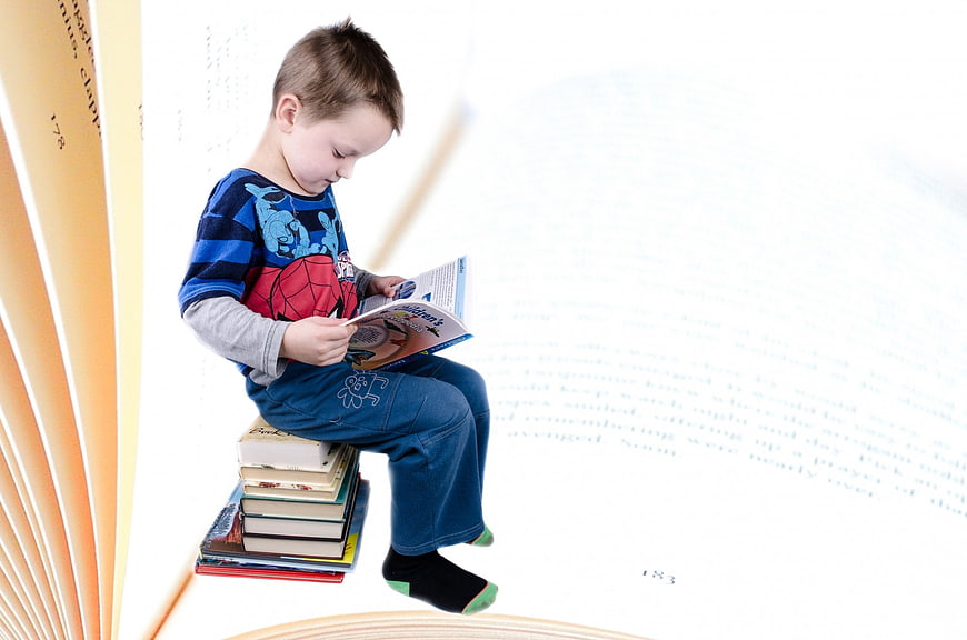 Young boy reading a book while sitting on a stack of books