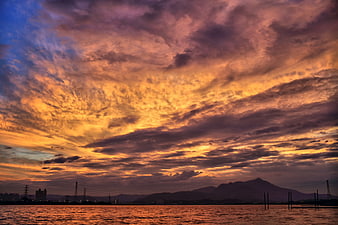 Dramatic sunset over water with mountain silhouette and vibrant clouds