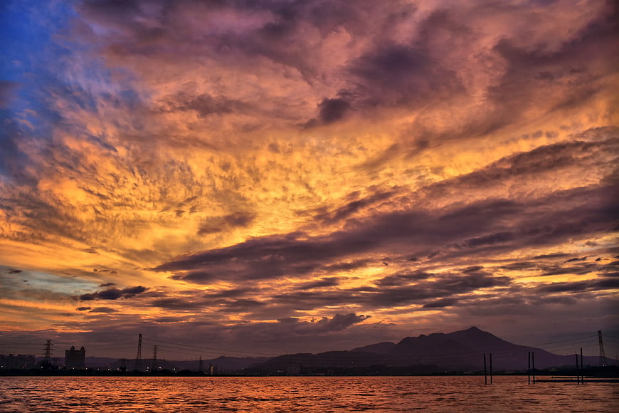 Dramatic sunset over water with mountain silhouette and vibrant clouds