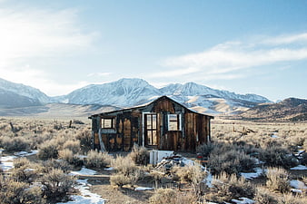 Derelict wooden cabin in a snowy desert landscape with mountains