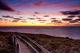Wooden boardwalk leading to ocean sunset with colorful sky