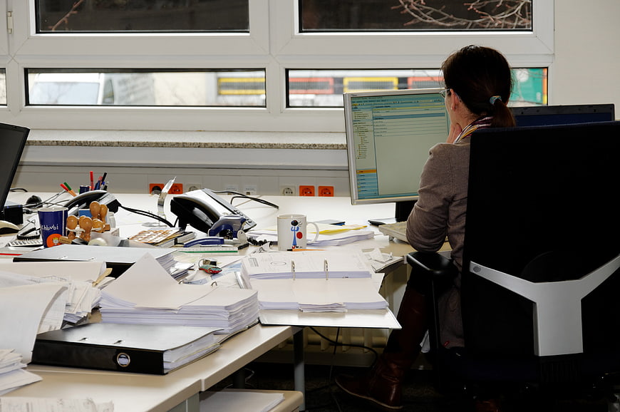 Woman Working At Cluttered Office Desk With Computer Monitor