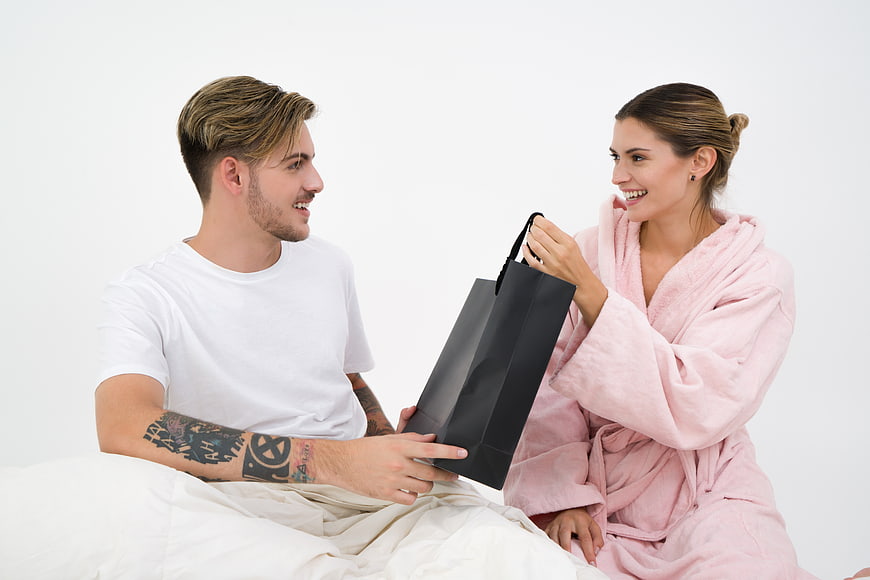 Happy couple in bed opening a black gift bag