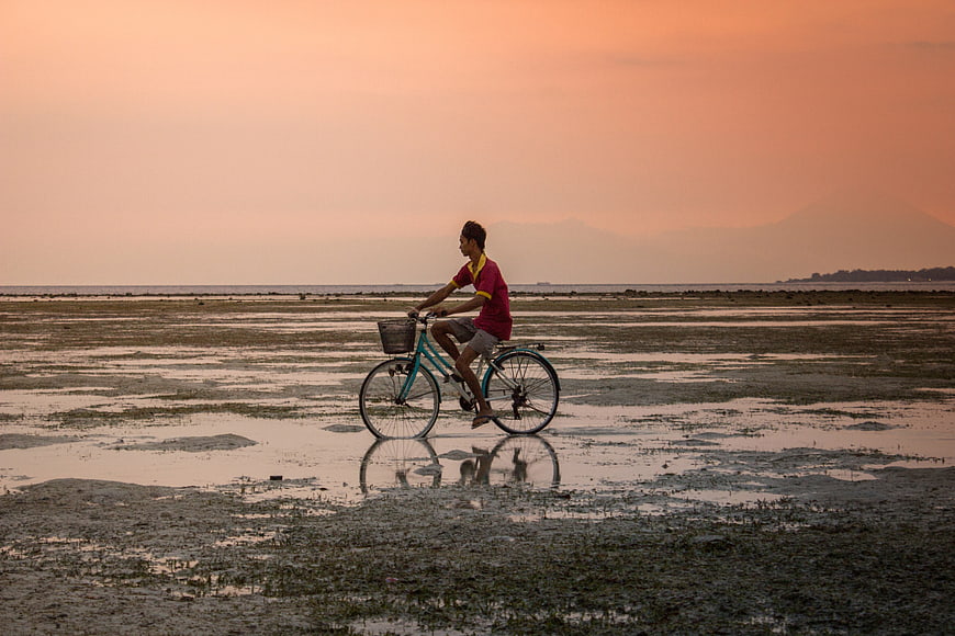 Man Cycling on Mudflats at Sunset with Mountain Reflection