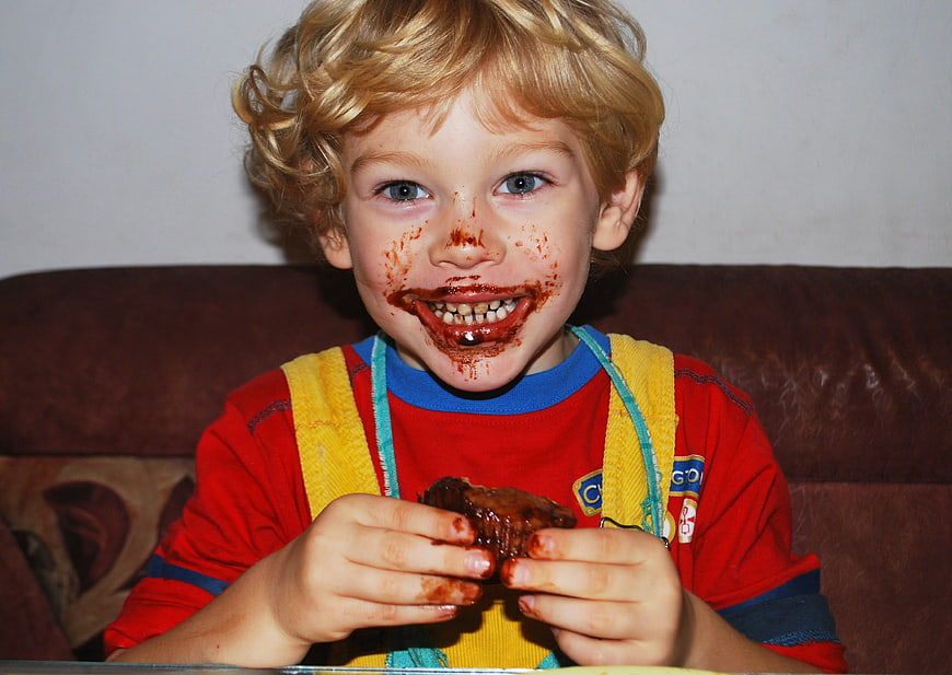Happy child eating chocolate muffin with messy face