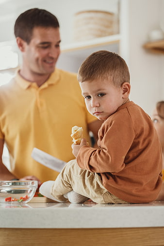 Toddler eating bread in kitchen with father