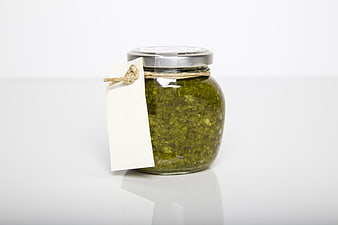 Glass Jar of Green Pesto Sauce with Blank Tag on White Background