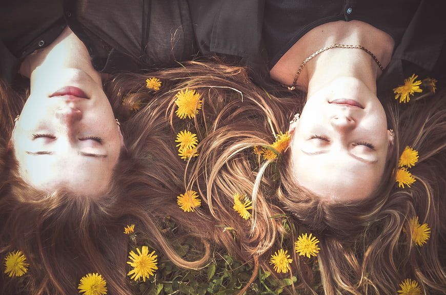 Two Women Lying In Grass With Dandelions