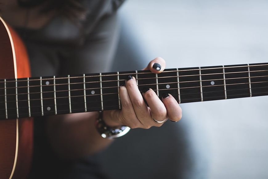 Close-up of woman playing acoustic guitar with black nail polish
