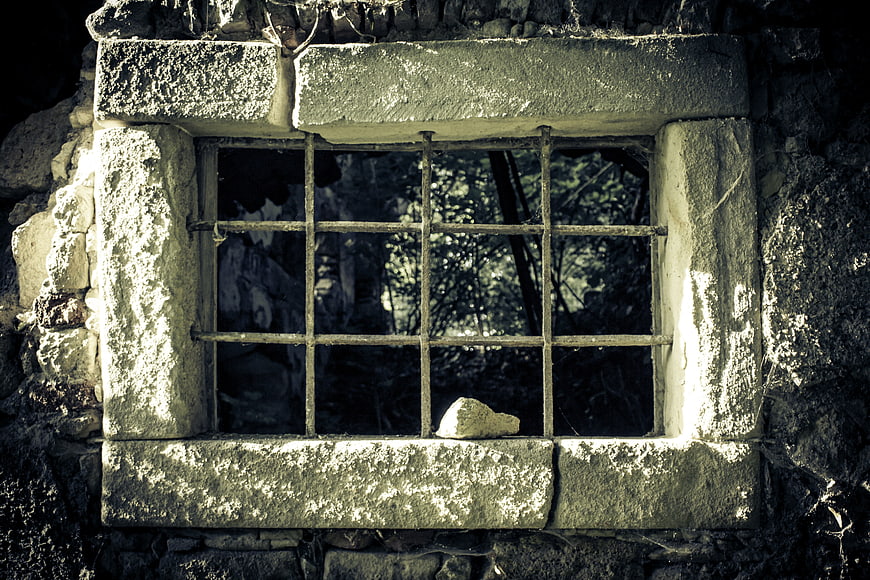 Old stone window with iron bars in abandoned ruin