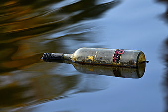 Dirty glass wine bottle floating in calm water