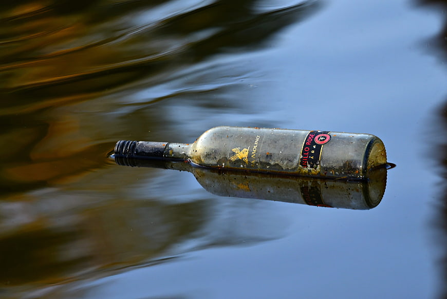 Dirty glass wine bottle floating in calm water