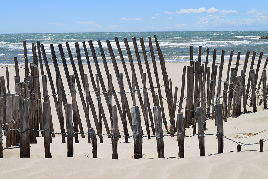 Weathered wooden dune fence on sandy beach with ocean waves