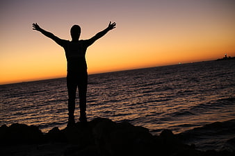 Silhouette of Man with Raised Arms at Sunset by the Sea