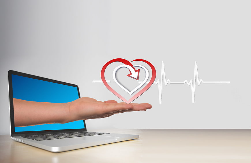 Hand holding heart icon and pulse line emerging from laptop screen