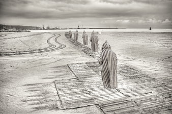 Striped hooded figures walking on wooden beach path