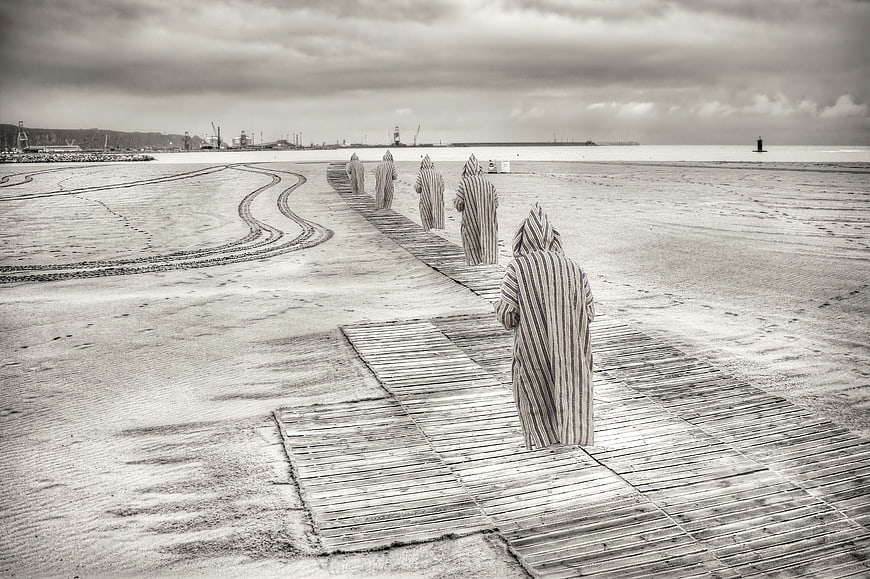 Striped hooded figures walking on wooden beach path