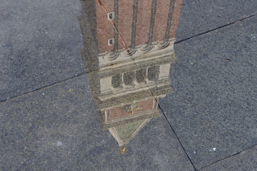 Reflection of brick bell tower in puddle on pavement