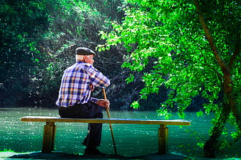 Senior man sitting on wooden bench by river in green forest
