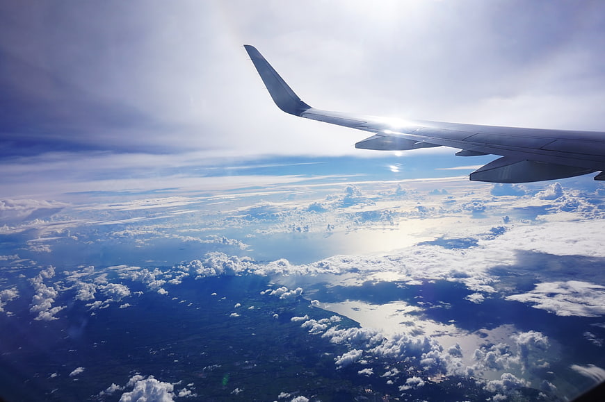 Airplane wing view over clouds and ocean landscape