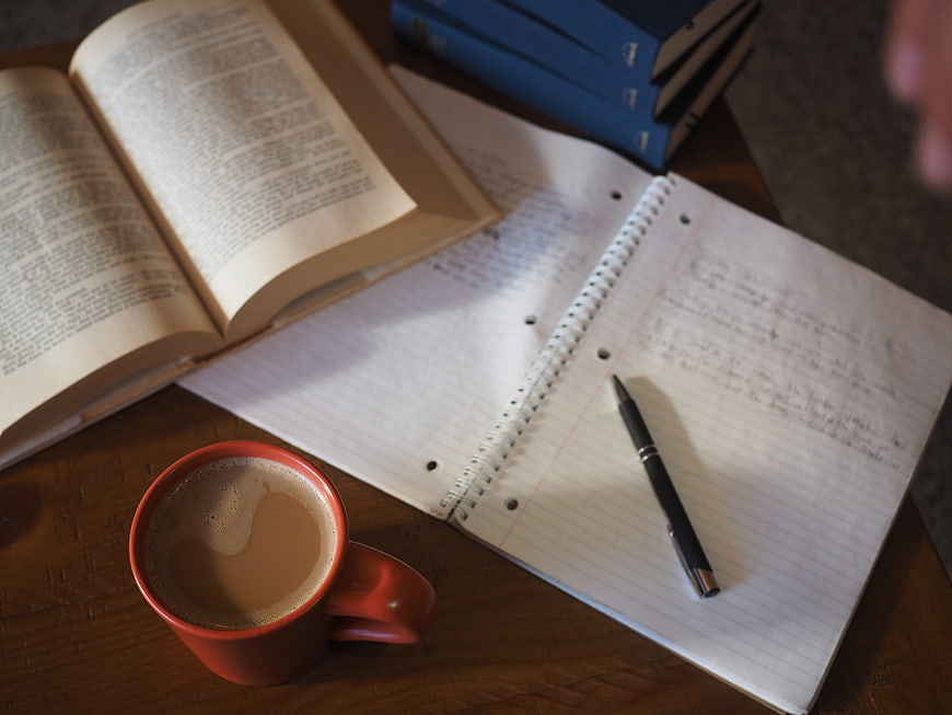 Study setup with coffee, notebook, and books on wooden table