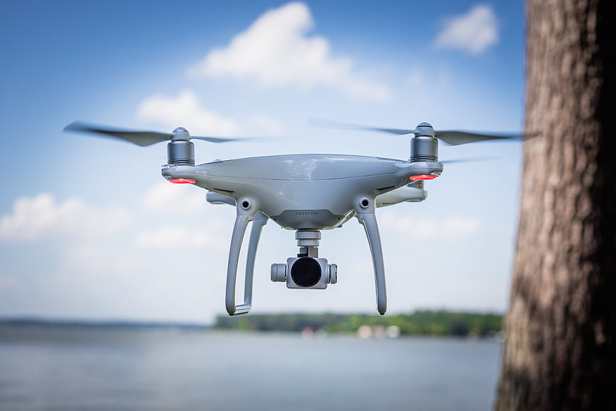 White DJI Phantom 4 Drone Hovering Over Lake With Blue Sky