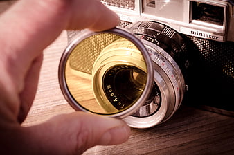Hand holding yellow filter over vintage camera lens
