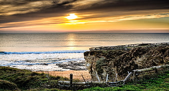 Dramatic sunset over ocean cliffs with wooden fence