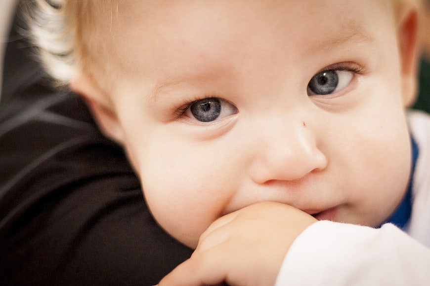 Close-up portrait of a baby with blue eyes resting chin on hand