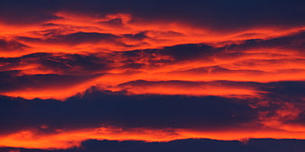 Dramatic fiery red and orange sunset clouds against dark blue sky