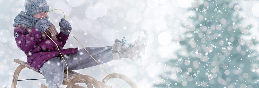 Child sledding in winter snow with festive bokeh background