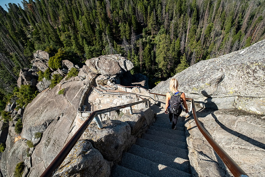 Woman hiking down steep mountain stairs with forest view