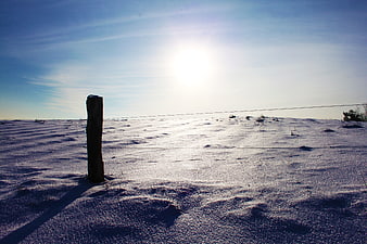 Lone wooden post in snowy landscape under bright sun
